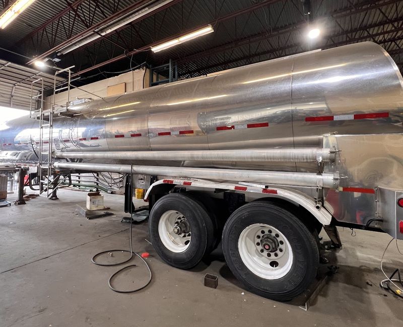 Tanker trailer in a shop bay, a hose on the floor and the ladder at the front.